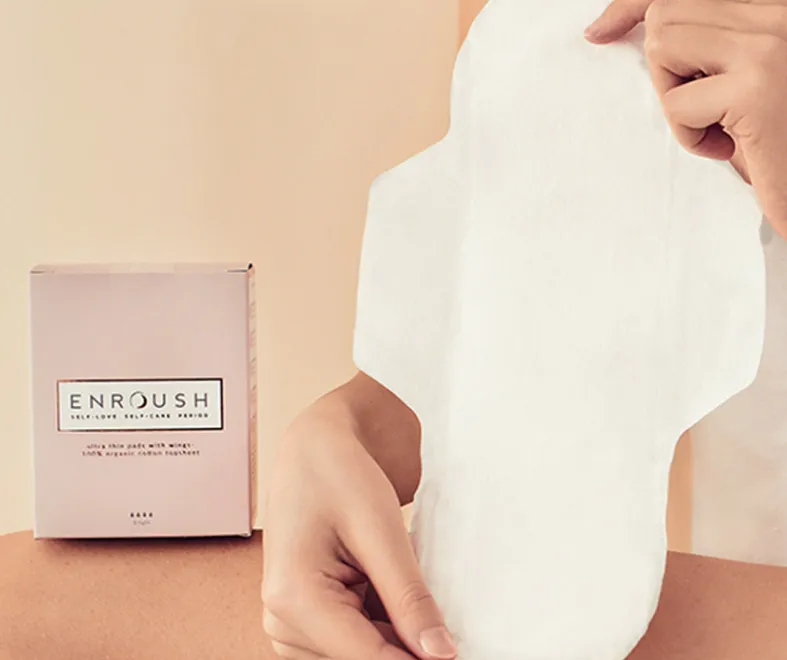 Hands gently pulling an Enroush organic cotton pad from its clean, minimal packaging